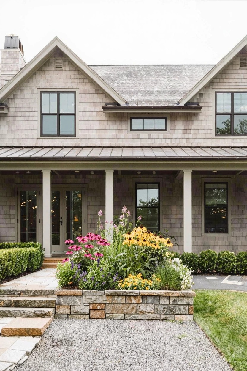 Modern white-walled courtyard with large rectangular white concrete planters filled with pink geraniums and trailing plants arranged around a central wooden bench on wet dark concrete paving.