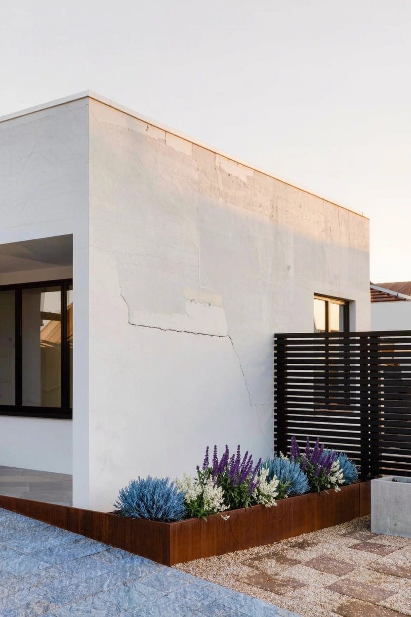 Mint green house with white porch, picket fence, and dense flower beds of pink and red roses along the fence line beside a brick pathway to the entry steps.