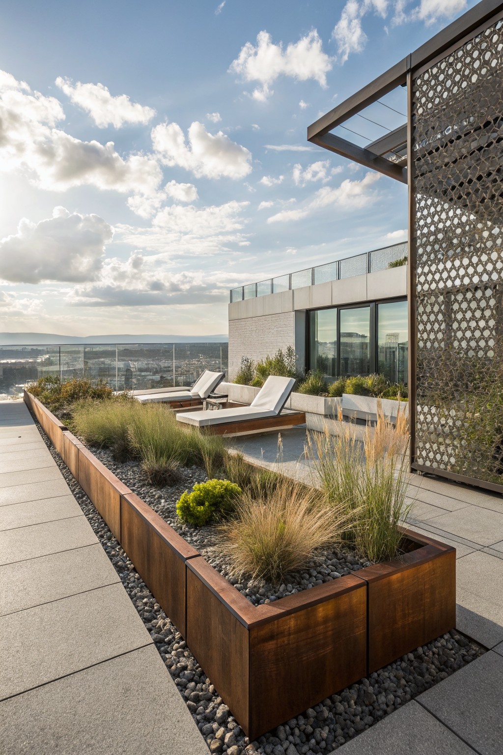 Rooftop terrace with linear corten steel raised planters filled with ornamental grasses and plants, two white lounge chairs, perforated metal screens, glass railings, and city skyline view in the background.