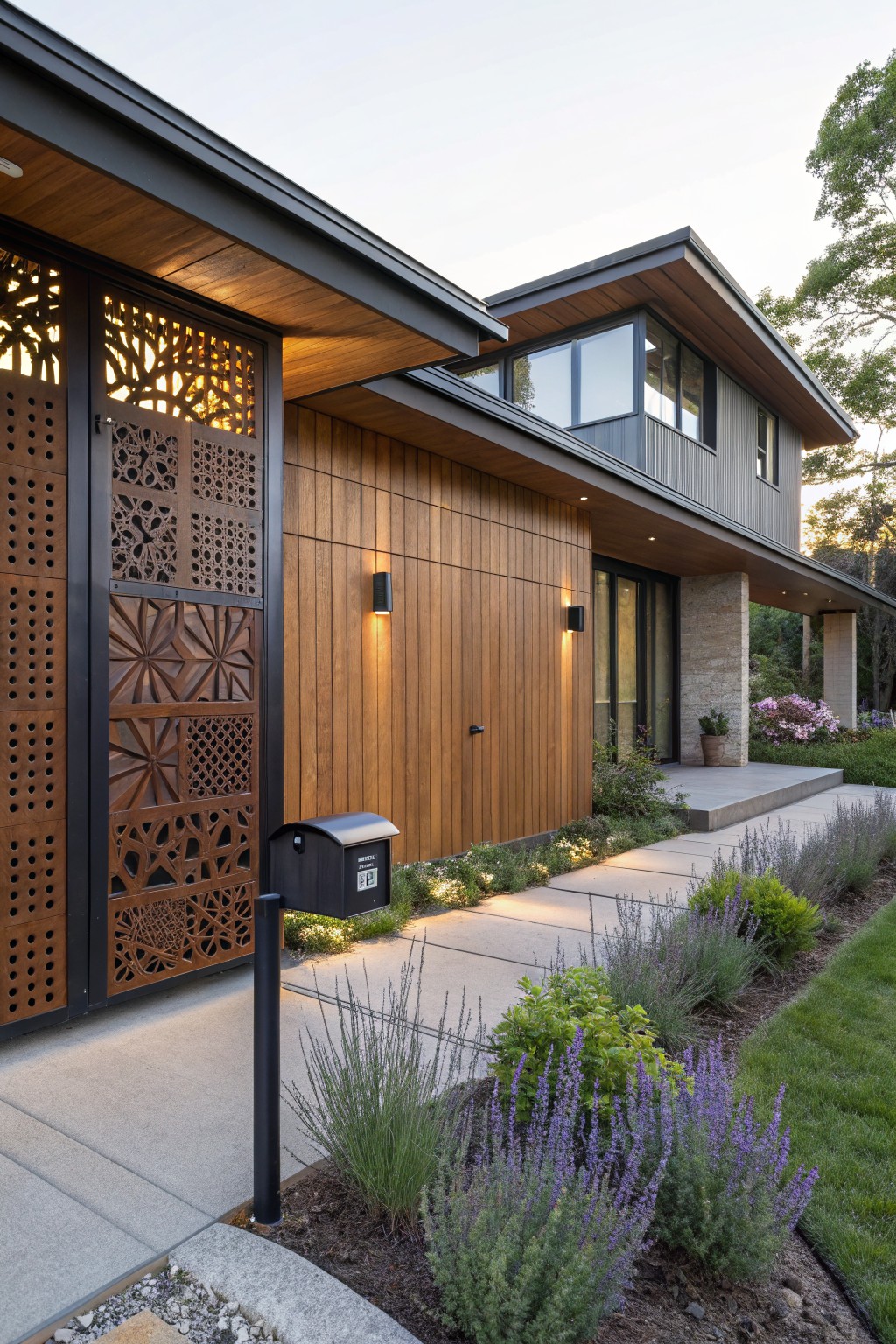 Modern house exterior with tall black perforated metal screen showing intricate cutout designs next to wood garage door, pathway lights, mailbox, and landscaped border with lavender plants.