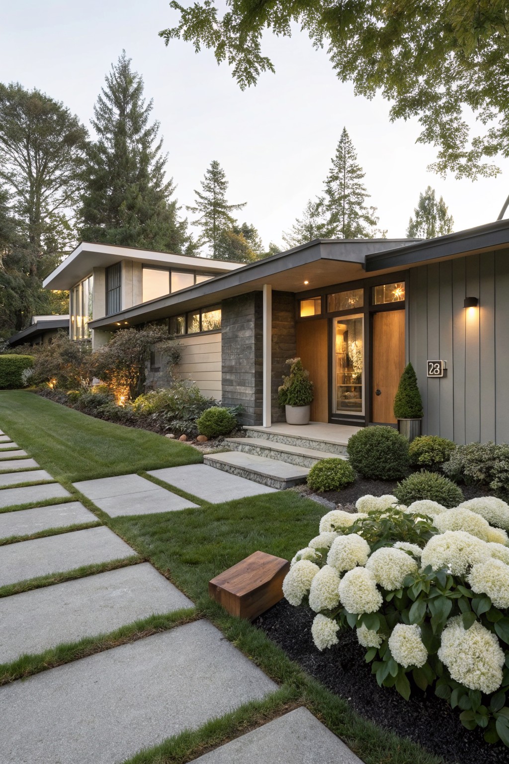 Modern gray house exterior with concrete paver pathway through green lawn leading to entry steps, edged by white hydrangea bushes, shrubs, and trees in background.