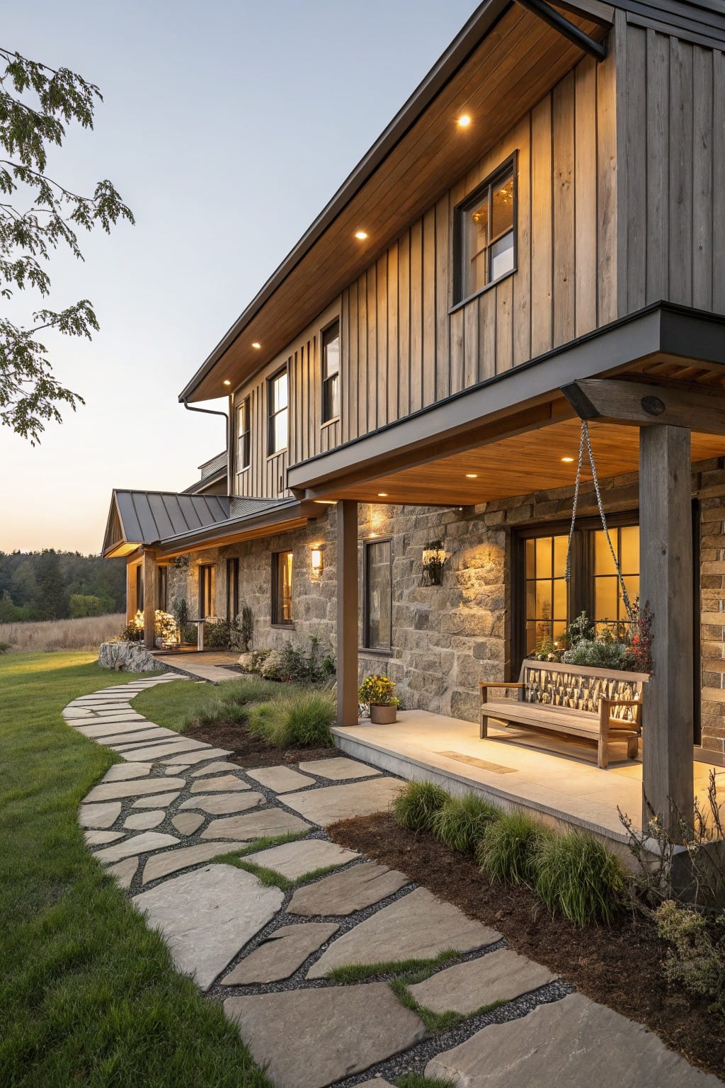 Side view of a two-story rustic house with vertical wood siding and metal roof, covered porch on stone pillars with wooden swing and bench, winding stone pathway through grass and plants at dusk.