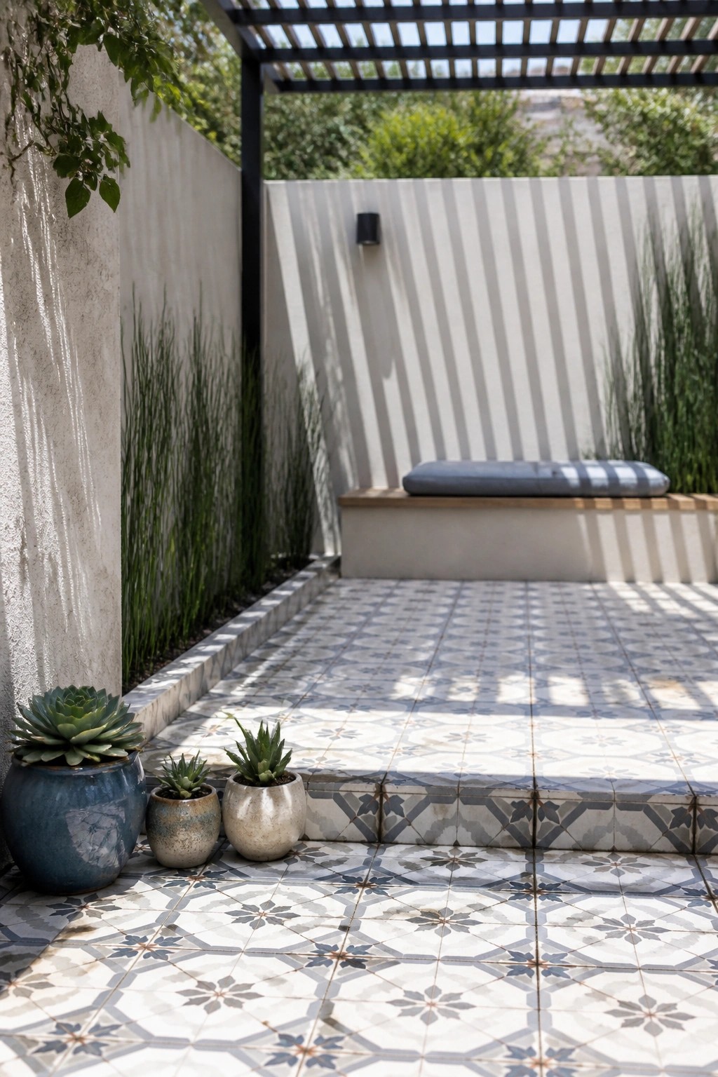 Tiled patio with potted succulents, tall grasses, built-in bench, and overhead pergola.