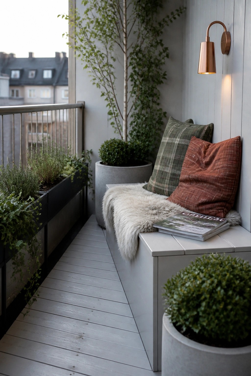A narrow balcony with a long built-in bench, cushions, a sheepskin throw, stacked magazines, and multiple potted plants along the wall.