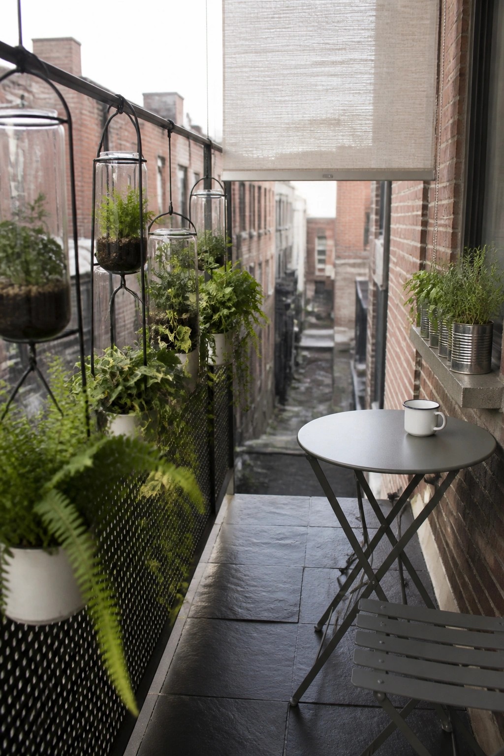 Urban balcony with hanging glass planters, ferns, round table, chair, and brick wall.