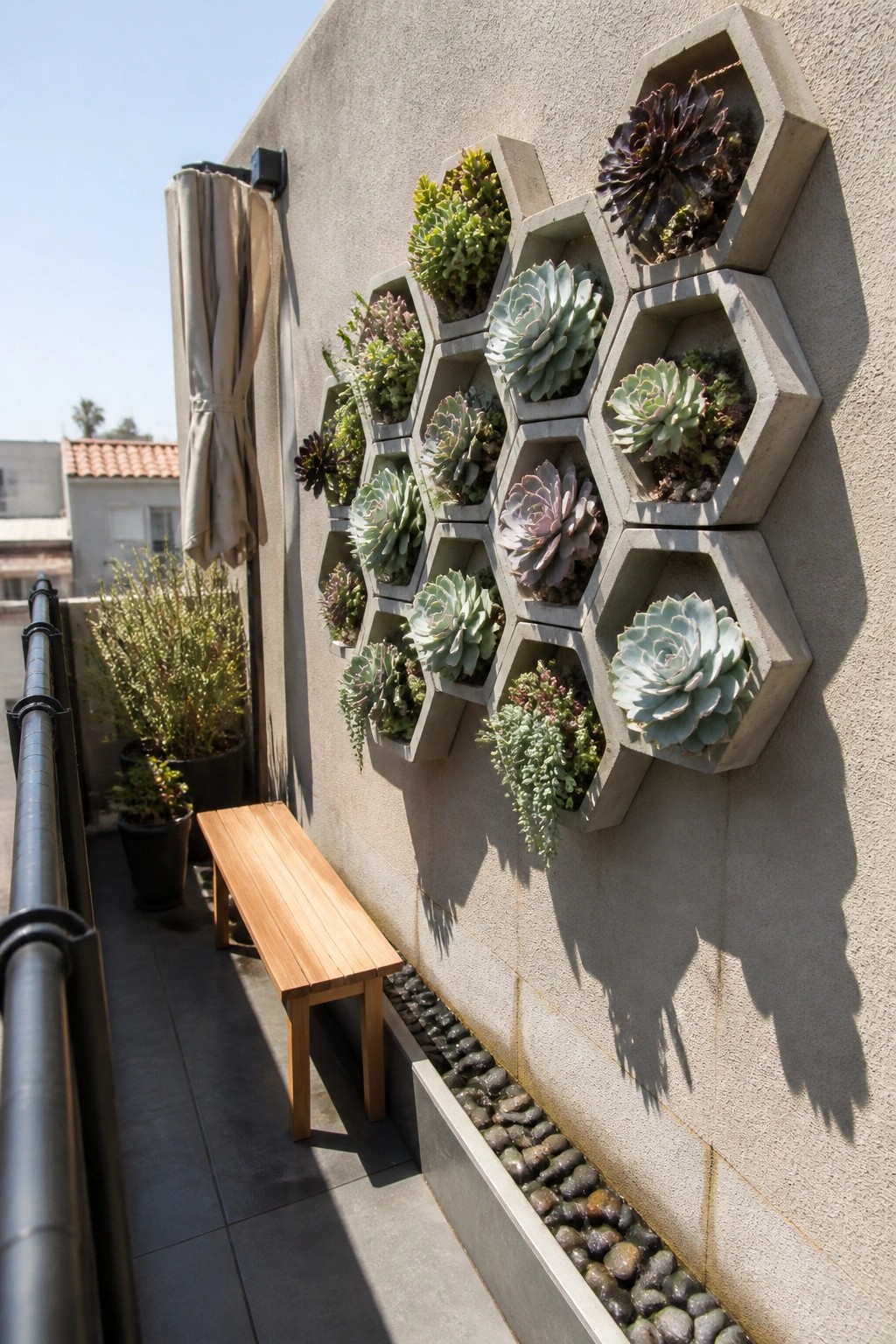 A balcony wall displays hexagonal concrete planters filled with succulents above a wooden bench and a pebble border.