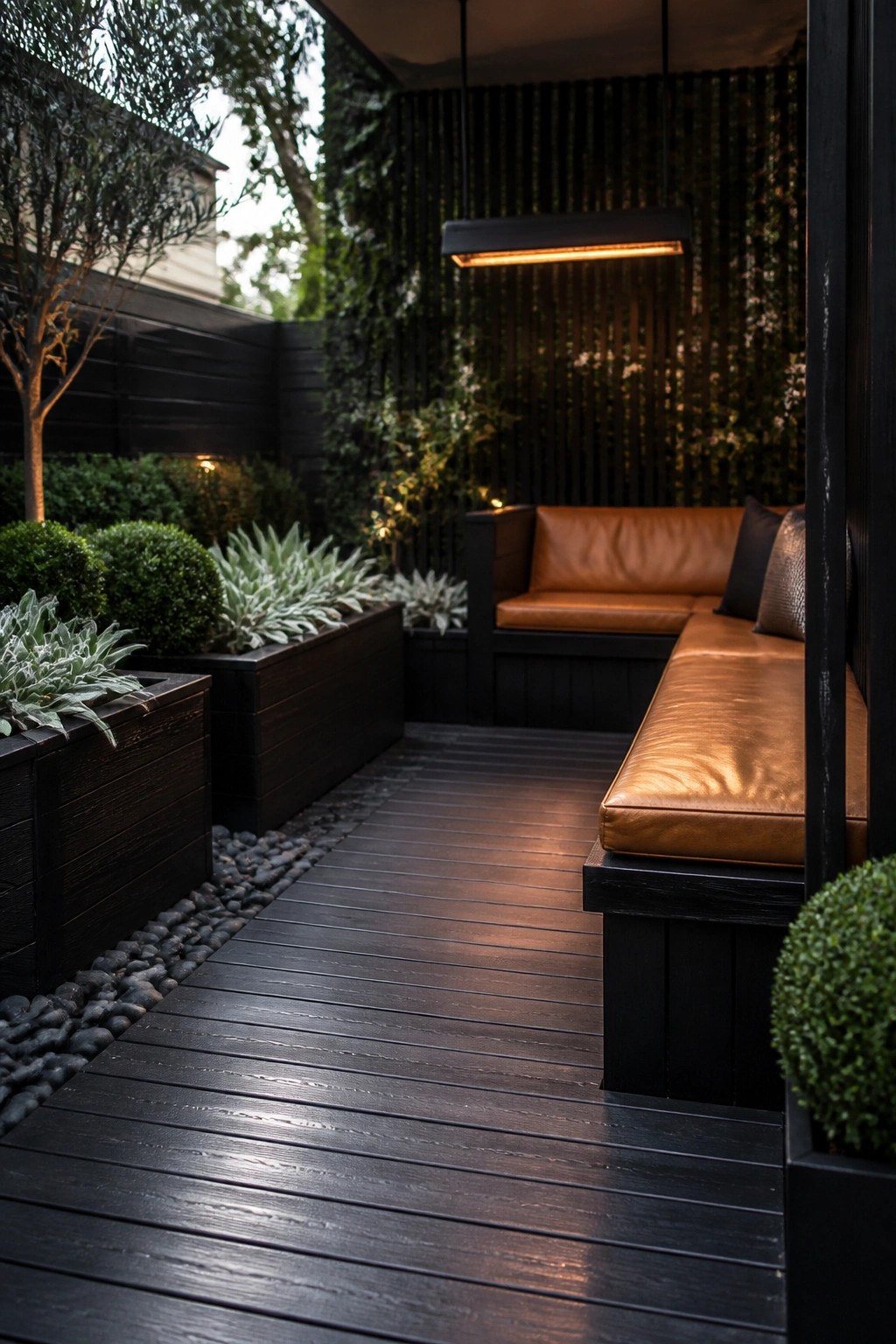 A narrow dark wood deck features built-in brown leather benches along the sides, with surrounding planters, gravel edging, and a single overhead light fixture.
