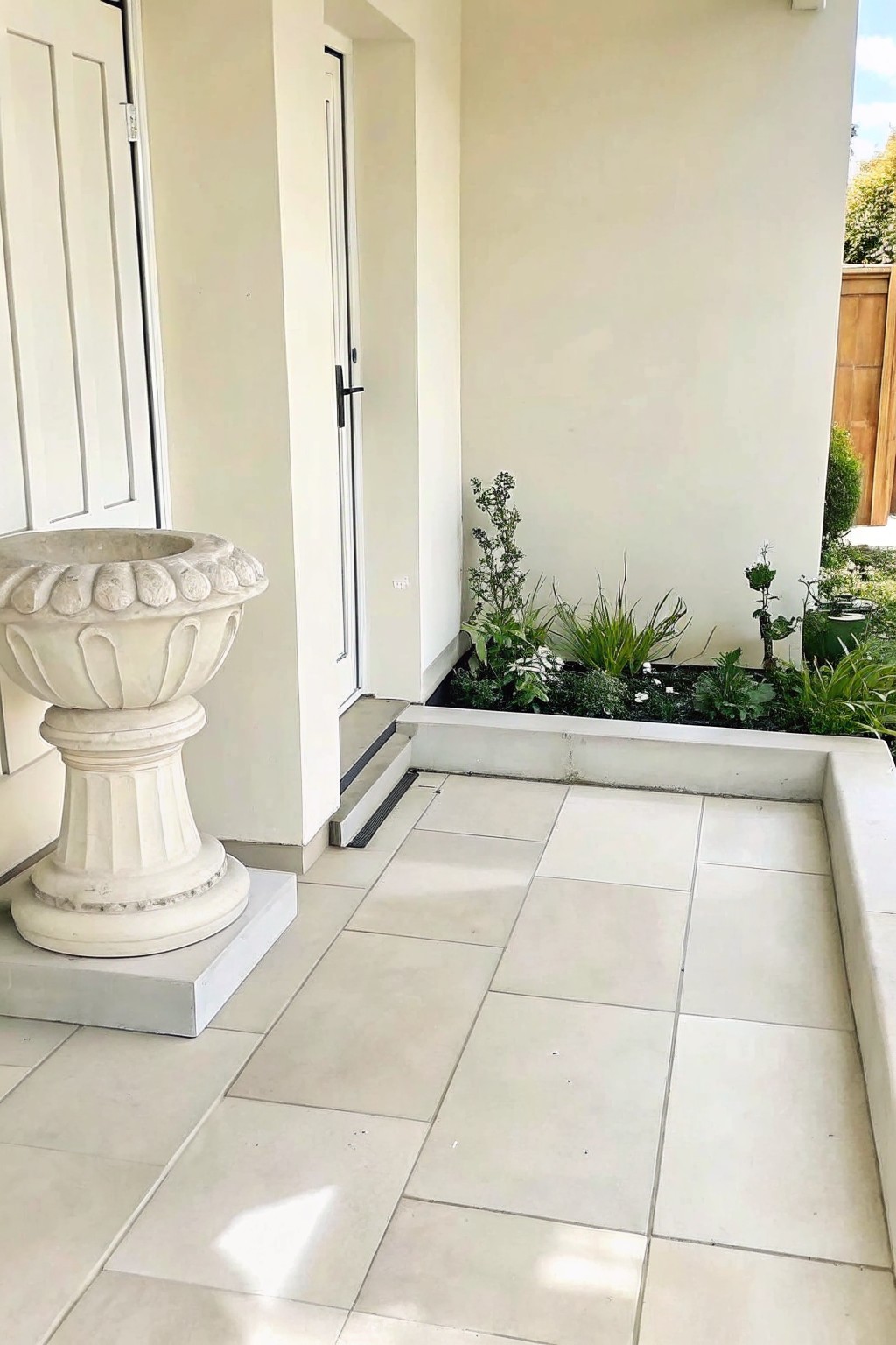 Tiled patio with white urn on pedestal and raised garden bed with plants