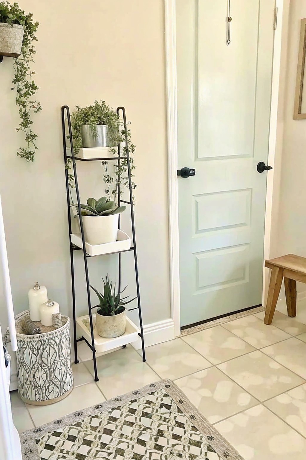 A black metal multi-tiered plant stand with several potted plants stands next to a light blue door in a tiled entryway.