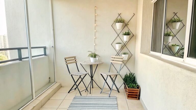 18 Renter-Friendly Garden Decor Ideas Without Permanent Installation A narrow balcony with a white round table, two woven chairs, a black metal grid holding potted plants, hanging lanterns on the wall, and a striped rug on the tiled floor.