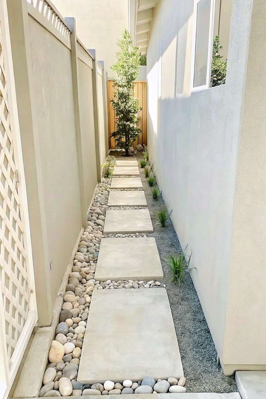 A narrow outdoor walkway made of rectangular concrete stepping stones set in a bed of pebbles, bordered by walls on both sides.