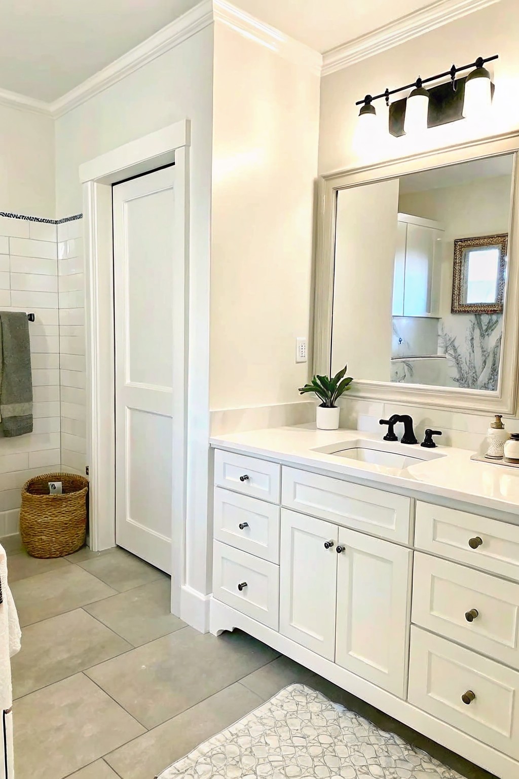 White bathroom vanity with black faucet, large mirror, plant, and tiled floor