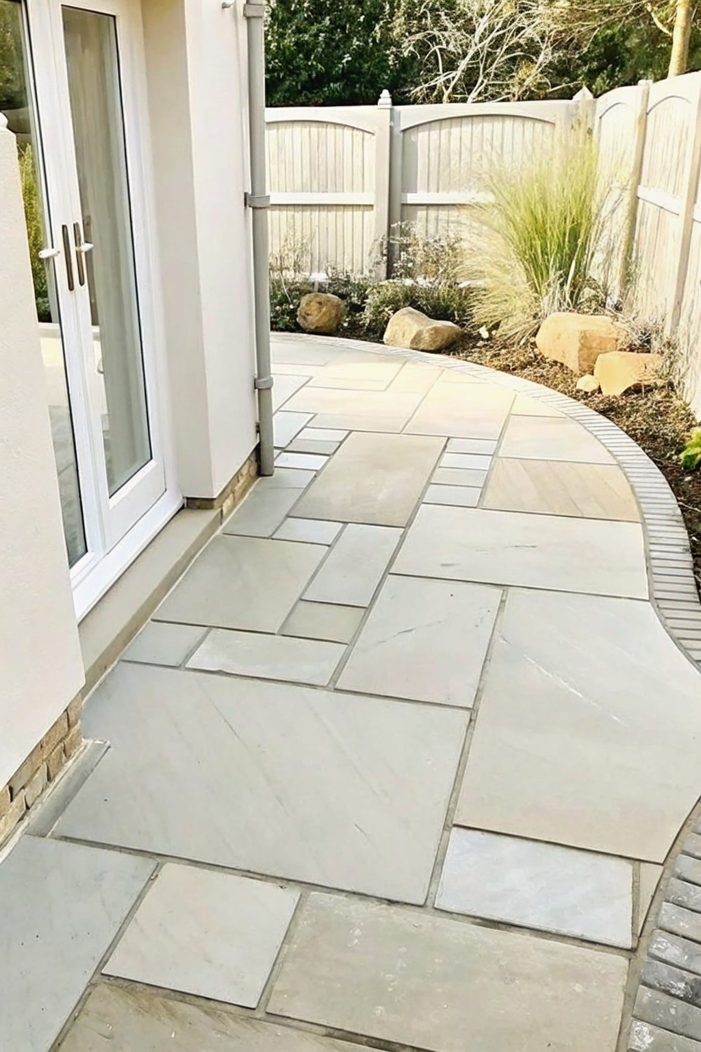 Curved stone patio with irregular tiles beside white doors and garden rocks.