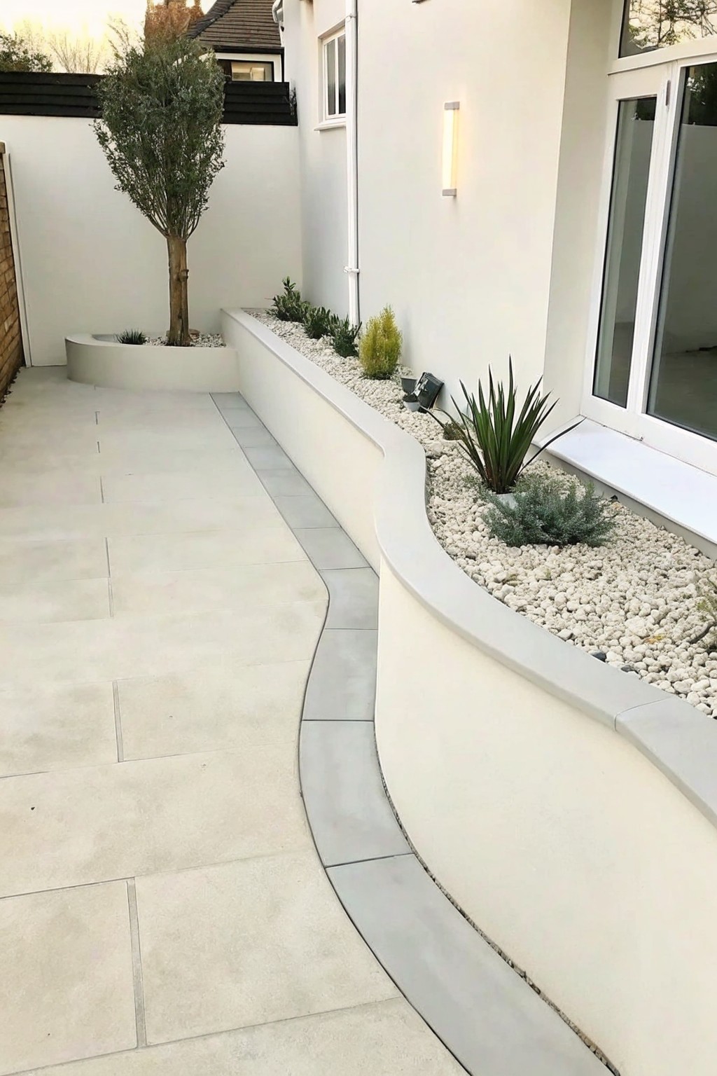 Modern courtyard with curved pebble-filled planter, plants, and light gray paving.