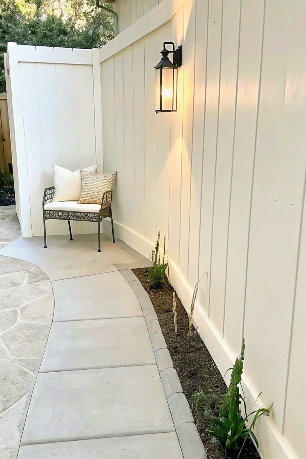Cozy patio nook with cushioned chair, pillow, and lit black lantern on fence