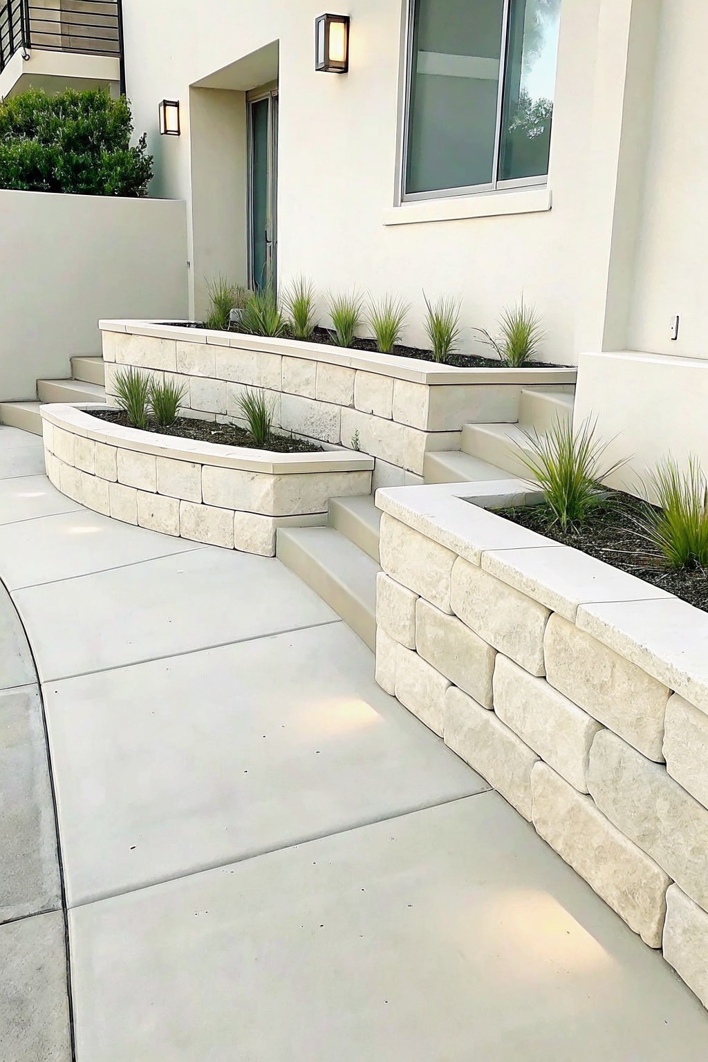 Modern white building with curved stone planters, steps, and ornamental grasses along walkway.