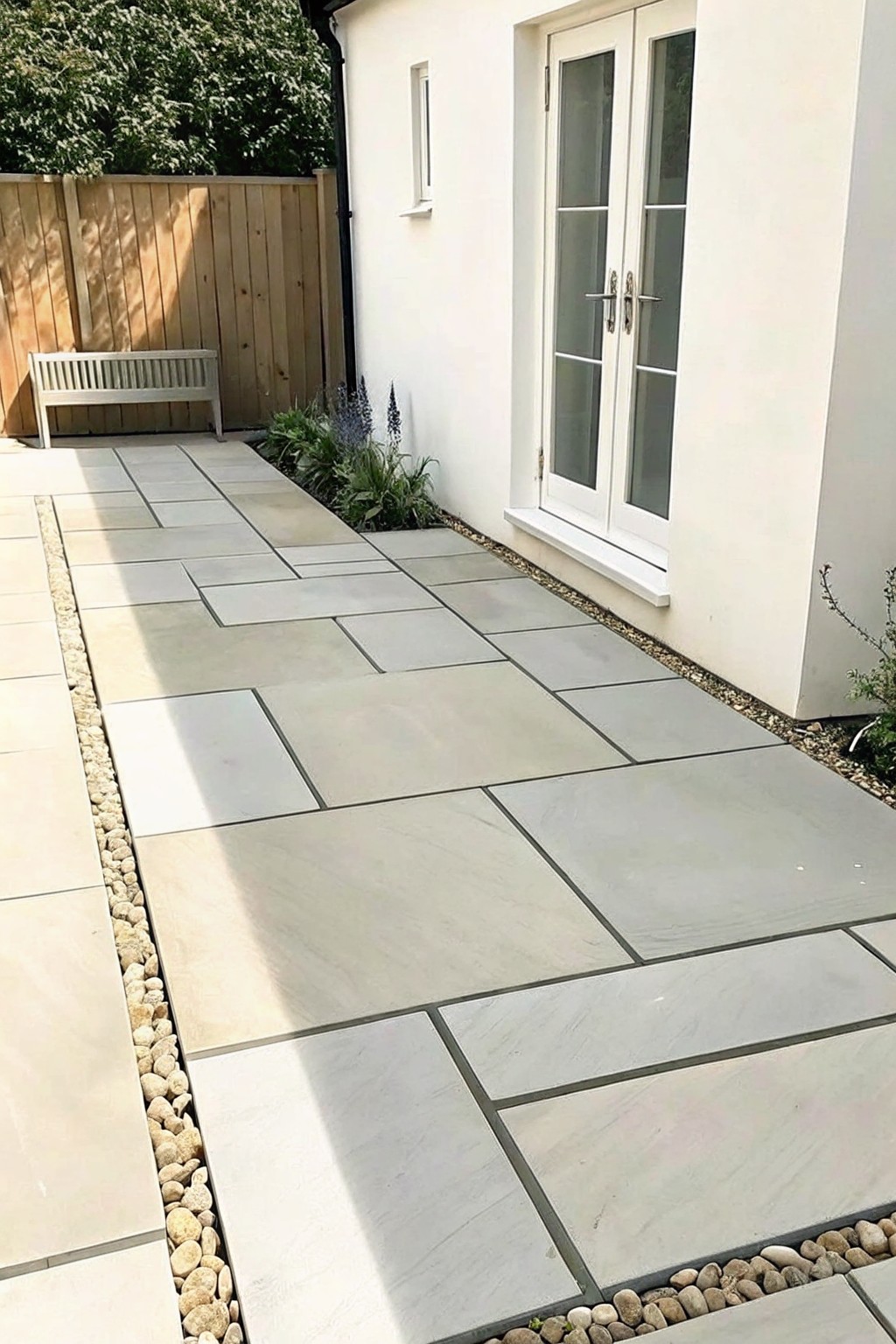 A stone slab path bordered by gravel runs alongside a white house wall with double doors.