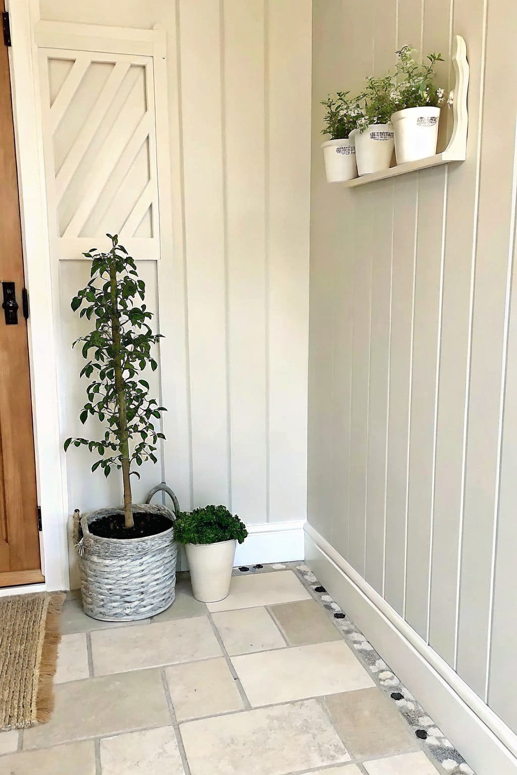 A light stone tile walkway with a narrow decorative pebble border running along the base of a gray wall, next to potted plants.