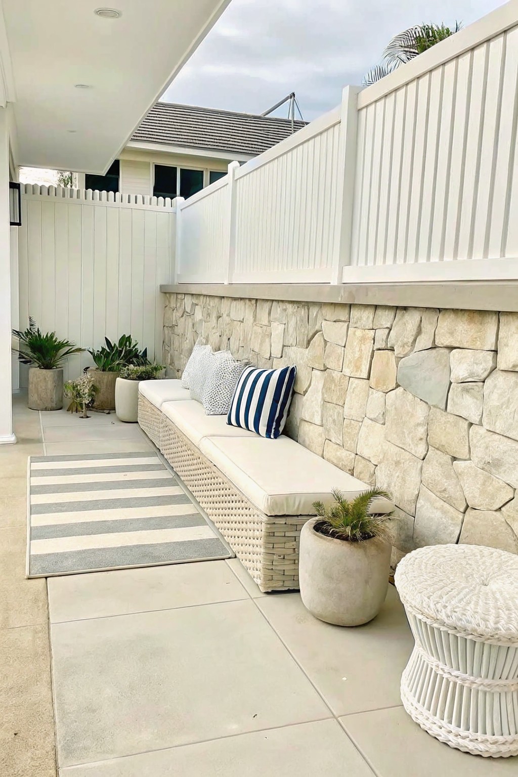 Modern patio with cushioned bench against stone wall, striped rug, and potted plants