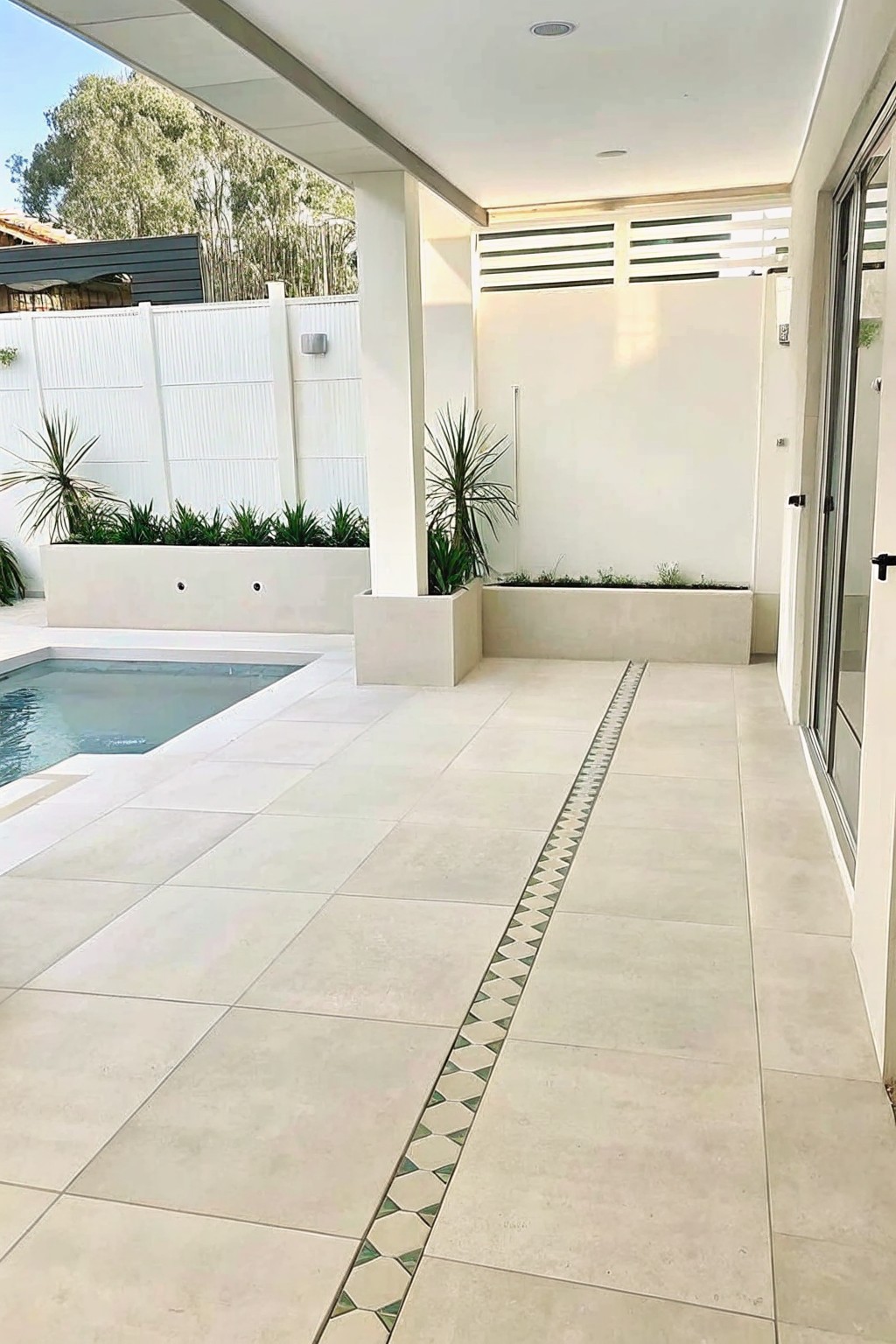 Tiled outdoor patio with swimming pool, concrete planters, and decorative border