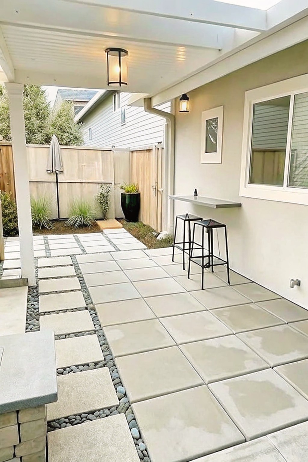 Modern backyard patio with light tiles, black bar stools, counter, and fence