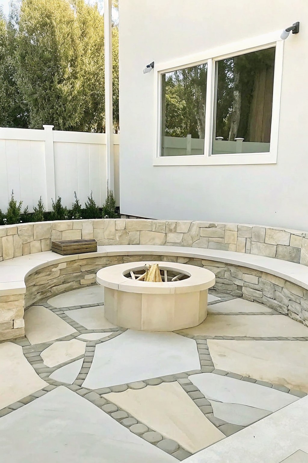 Round fire pit on patterned stone patio with curved bench and white wall