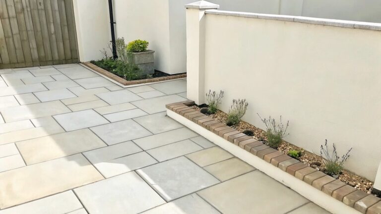 19 Space-Saving Garden Border Ideas for Narrow Beds and Small Yards A narrow paved walkway runs beside a white wall with a long raised garden bed edged in brick and planted with low shrubs and taller evergreens.