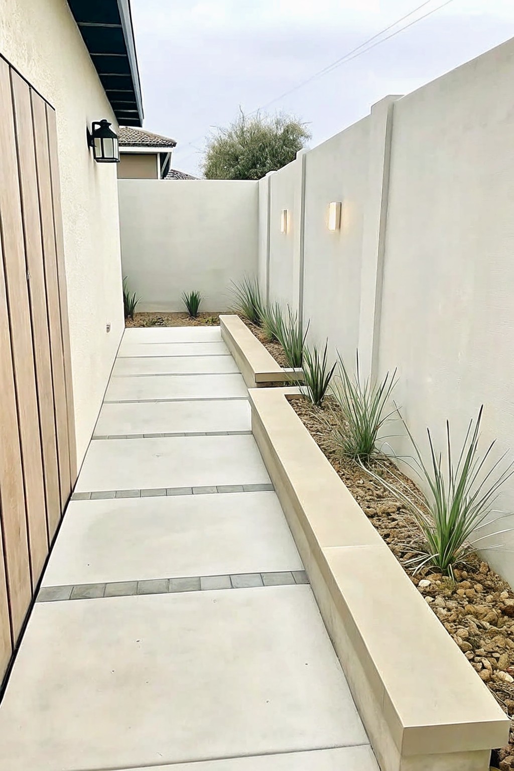 Narrow concrete path between white walls with built-in bench, gravel, and grasses