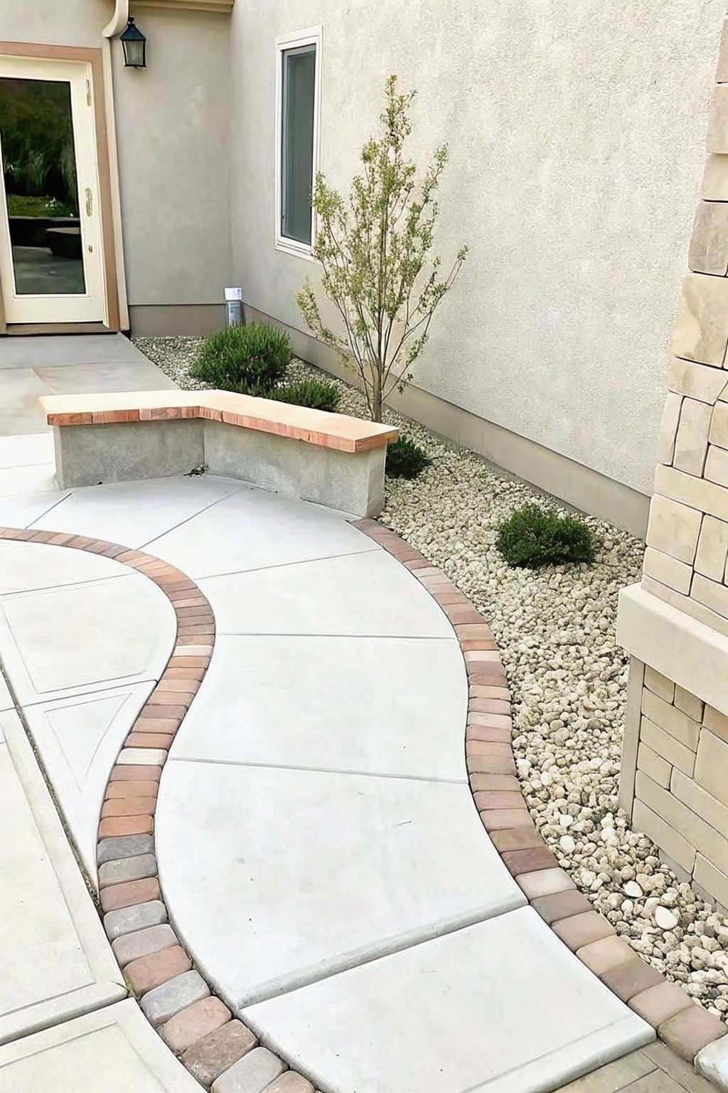 Curved concrete walkway with brick edging beside a bench and gravel garden.