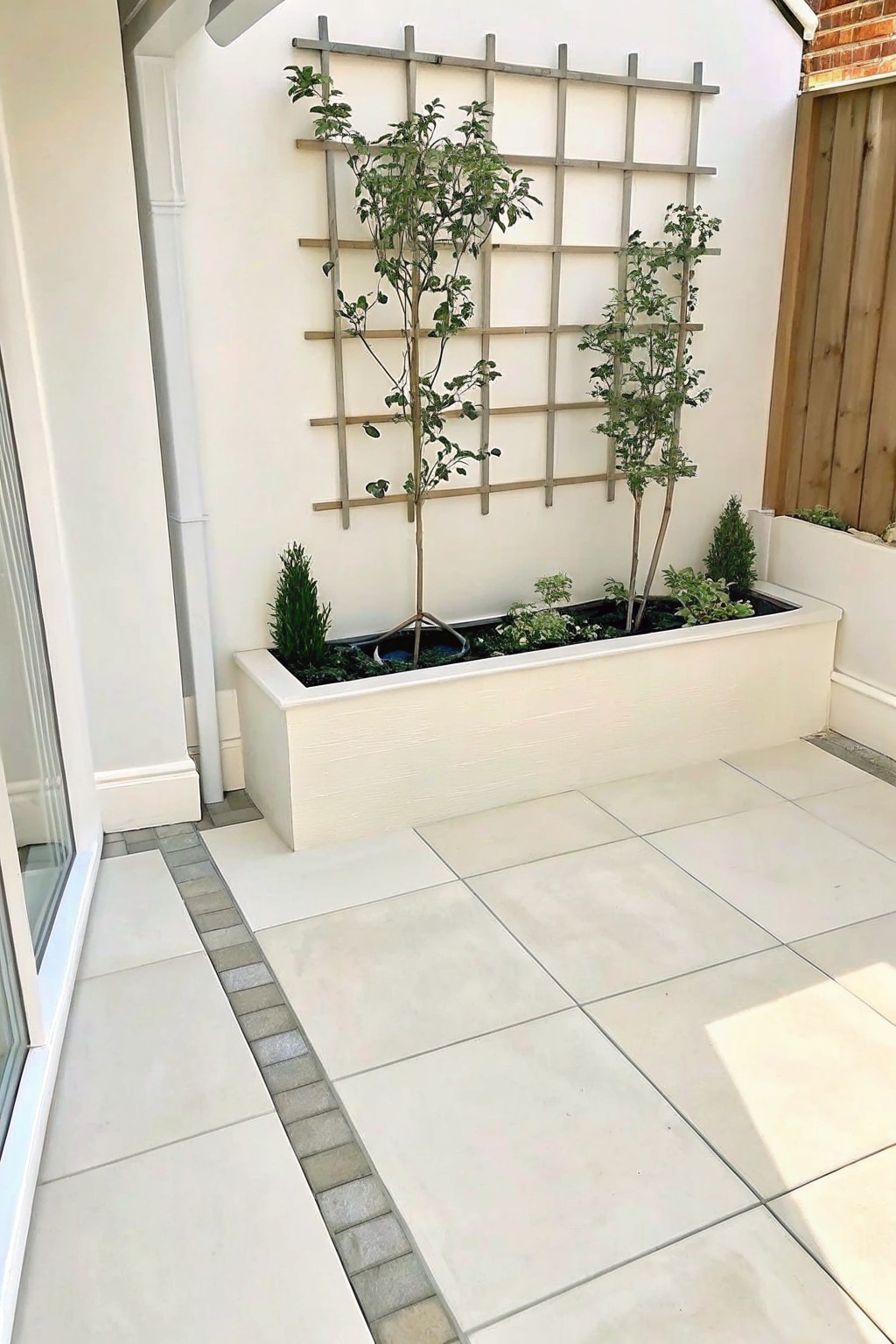 White planter with young trees and wooden trellis on patio wall