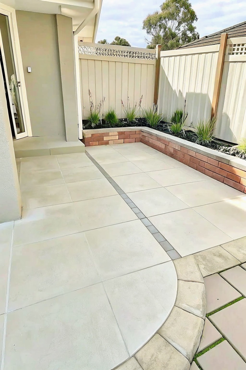 Spacious backyard patio with large light tiles, brick planter, and beige fence.