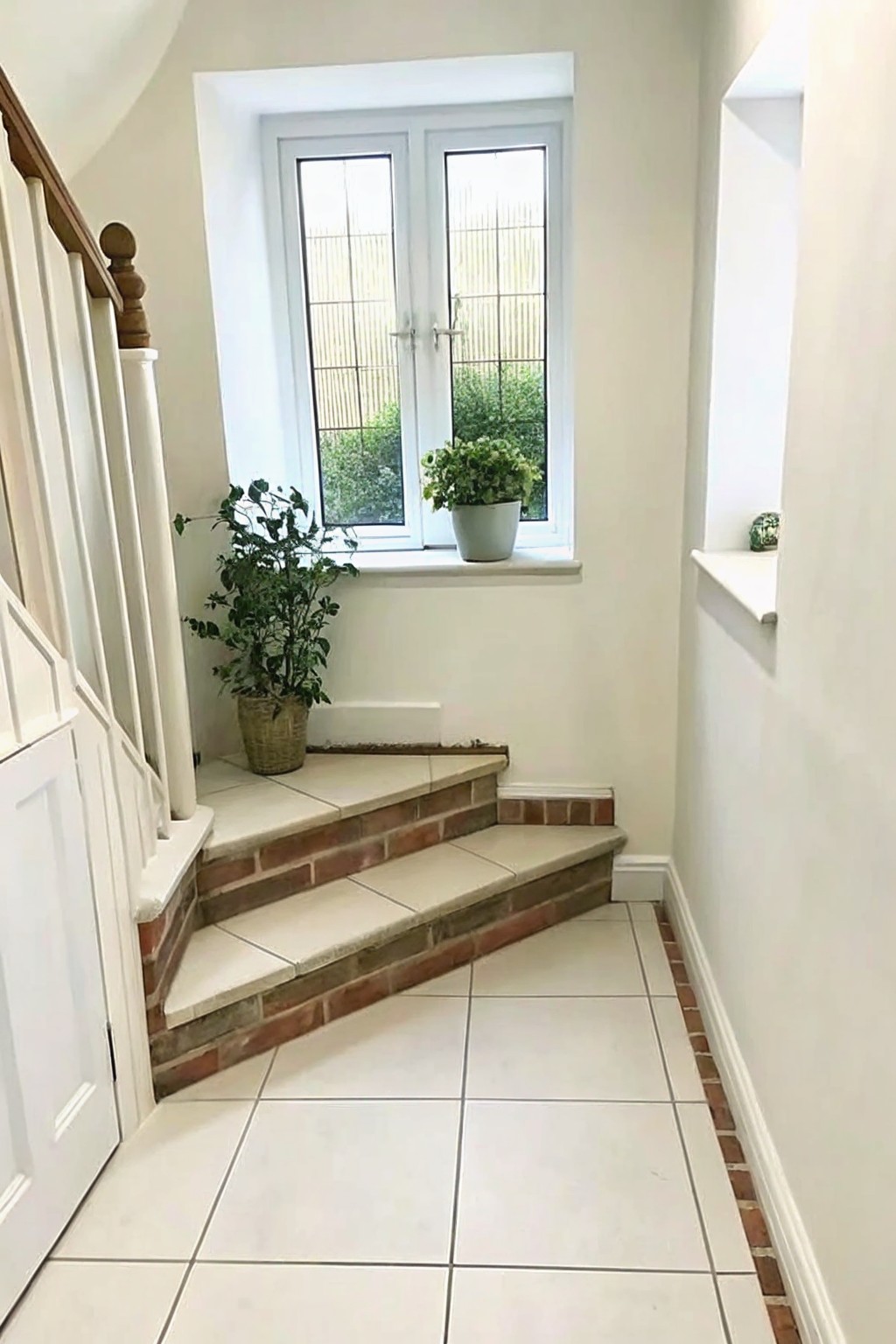 Indoor staircase with brick risers, beige tile treads, and potted plants near a window.
