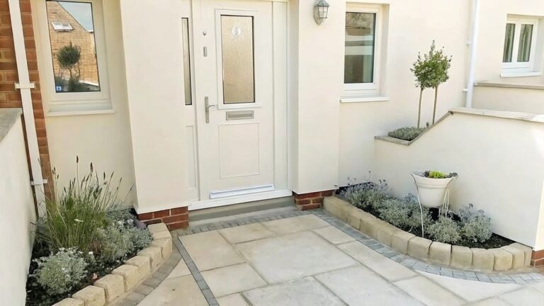 19 Timeless Brick Garden Borders for Curved and Traditional Flower Beds A stone paver path bordered by gravel and a low brick edge running along the base of a white house wall.