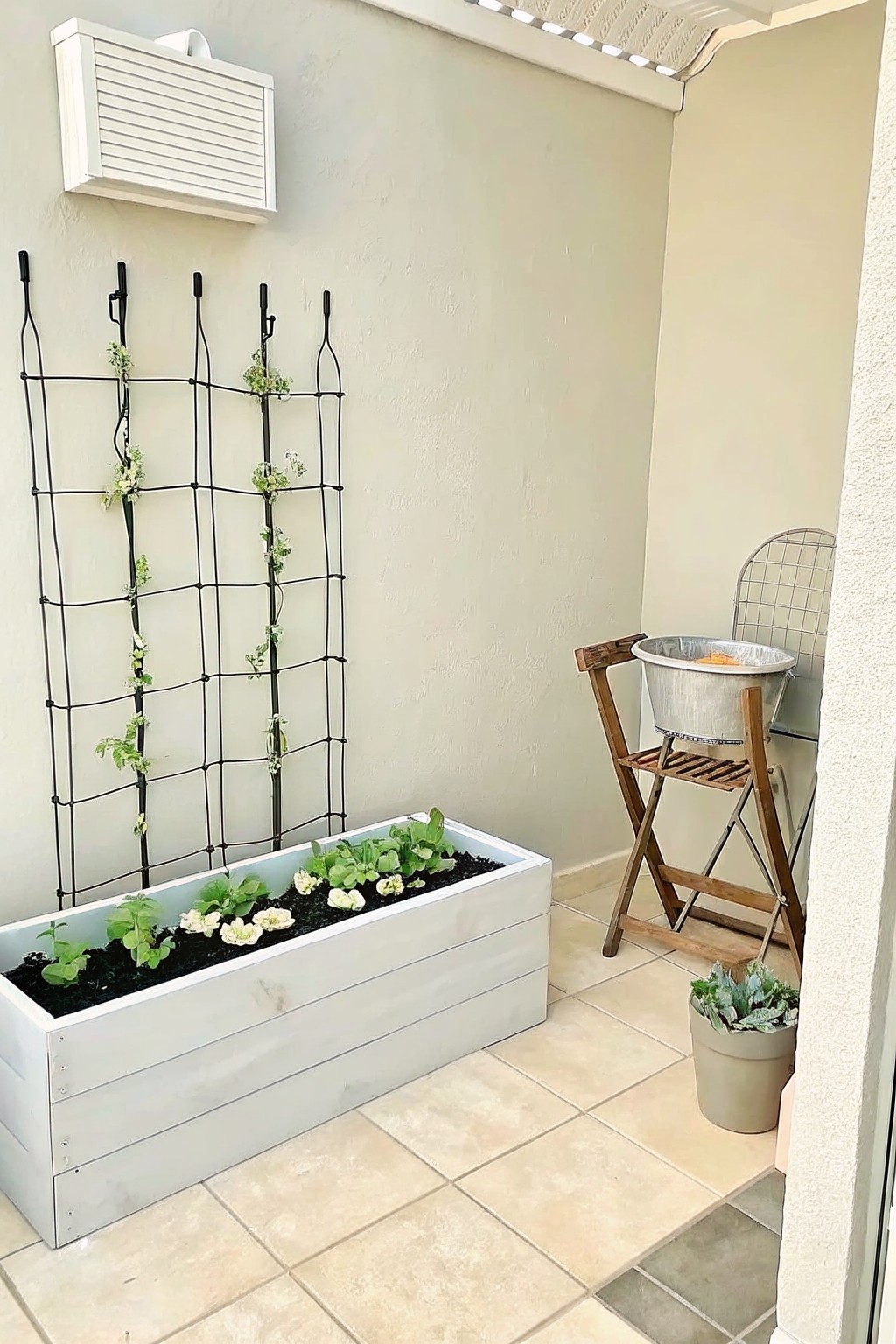 White planter box with greens and flowers beside black trellis on patio