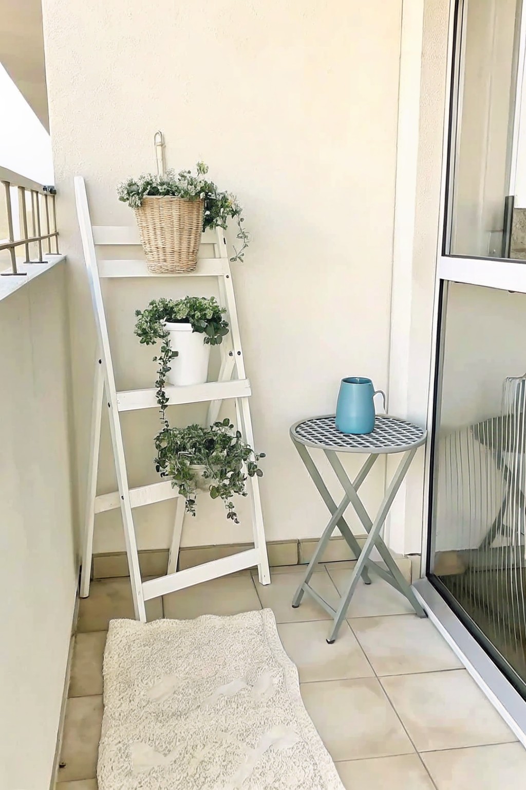 White ladder with hanging plants beside blue mug on small round table and lace rug.