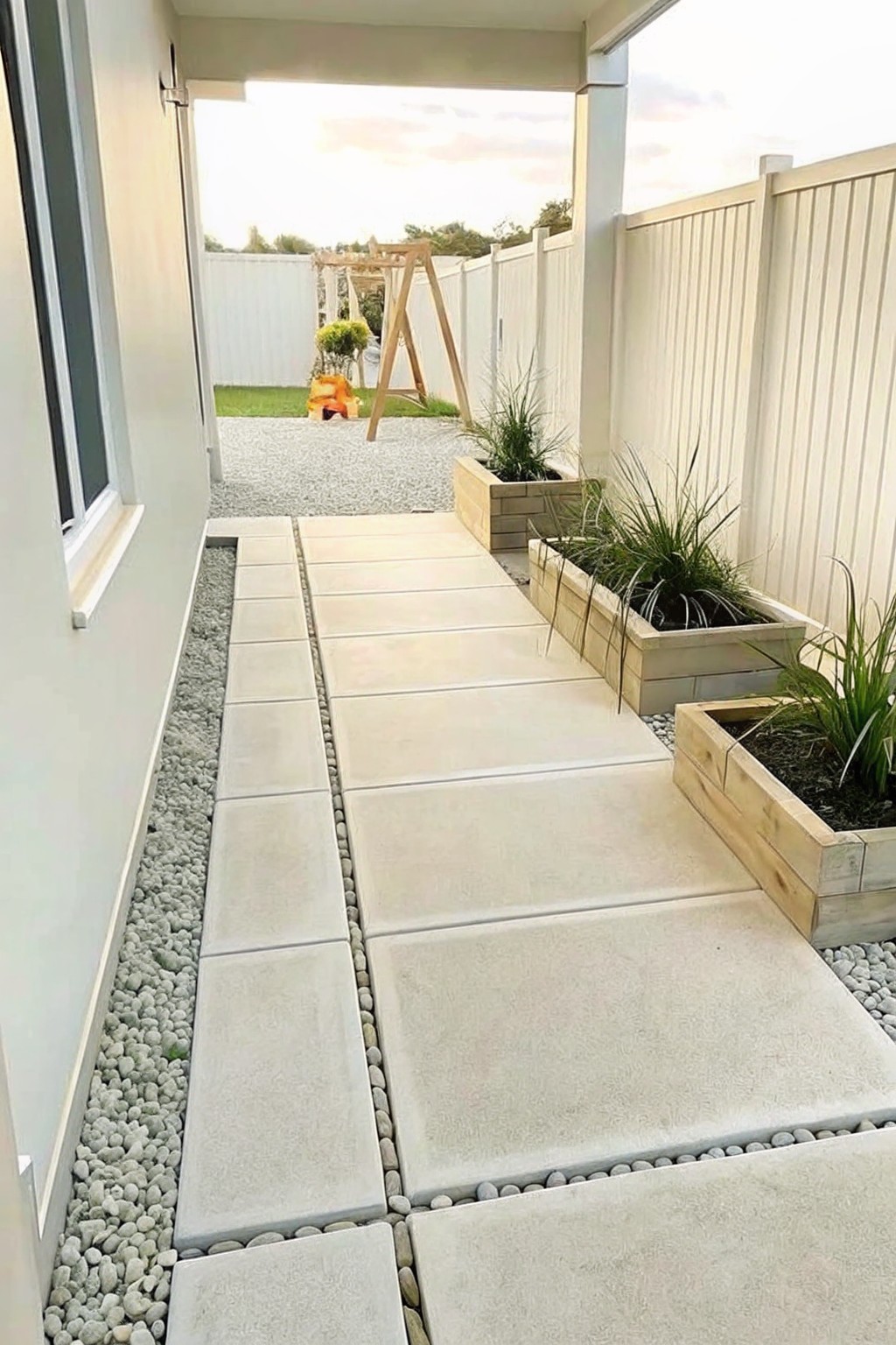 A straight concrete paver walkway bordered by gravel strips with wooden raised planter boxes along one side.