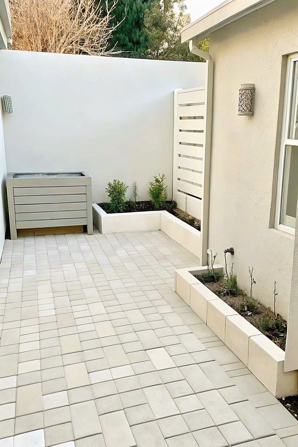 A paved courtyard with raised concrete planting beds along white walls and a small raised structure on the left.