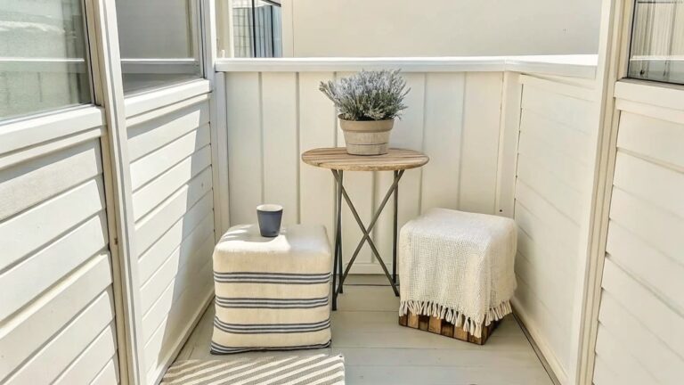 21 Chic Patio Garden Decor Ideas for Small Tables and Container Displays A narrow balcony shows a round wooden side table with a white potted plant, two woven poufs, and a metal railing along the right side.