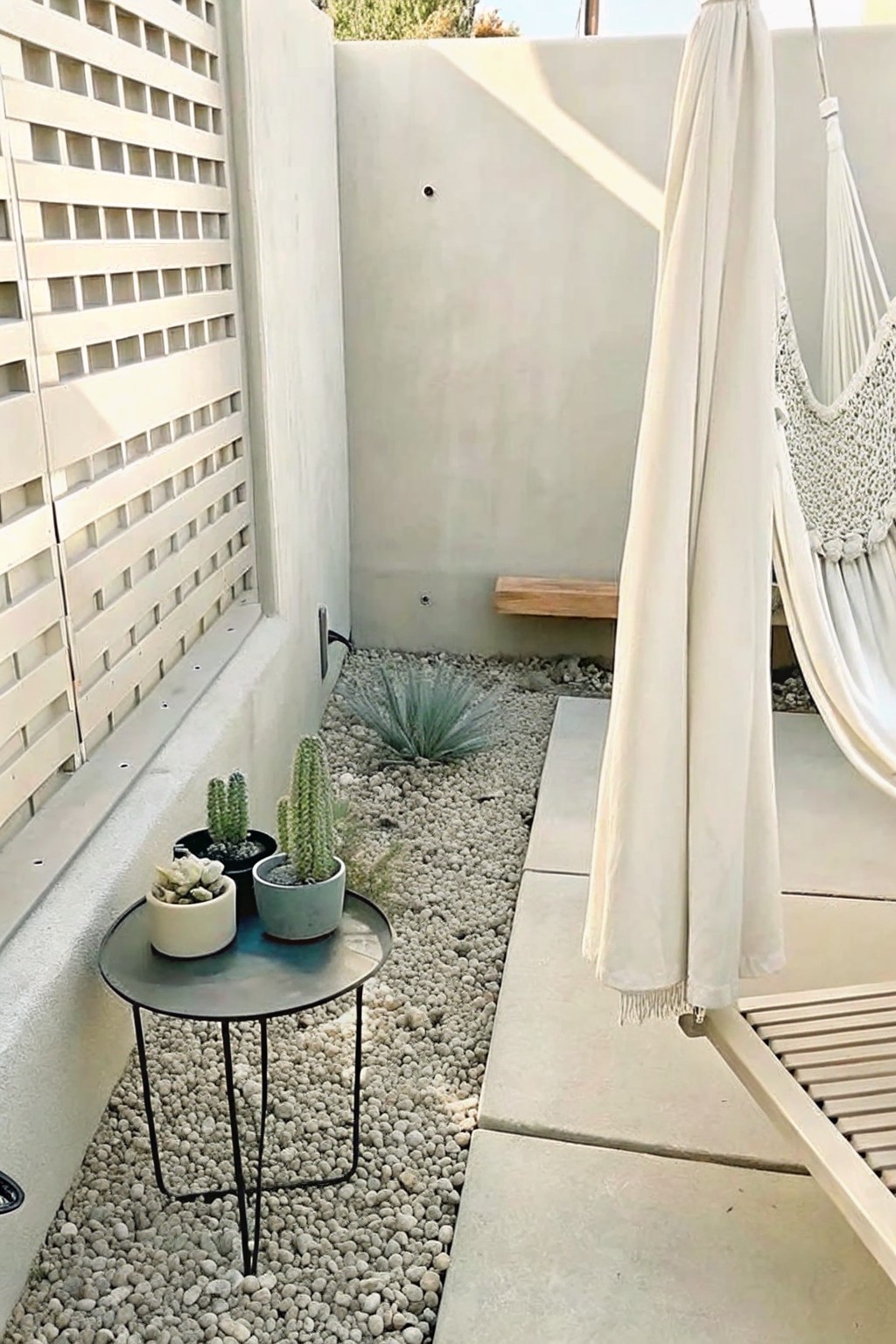 A small round metal table with four potted succulents and cacti sits on a gravel surface next to a concrete wall in an outdoor patio area.