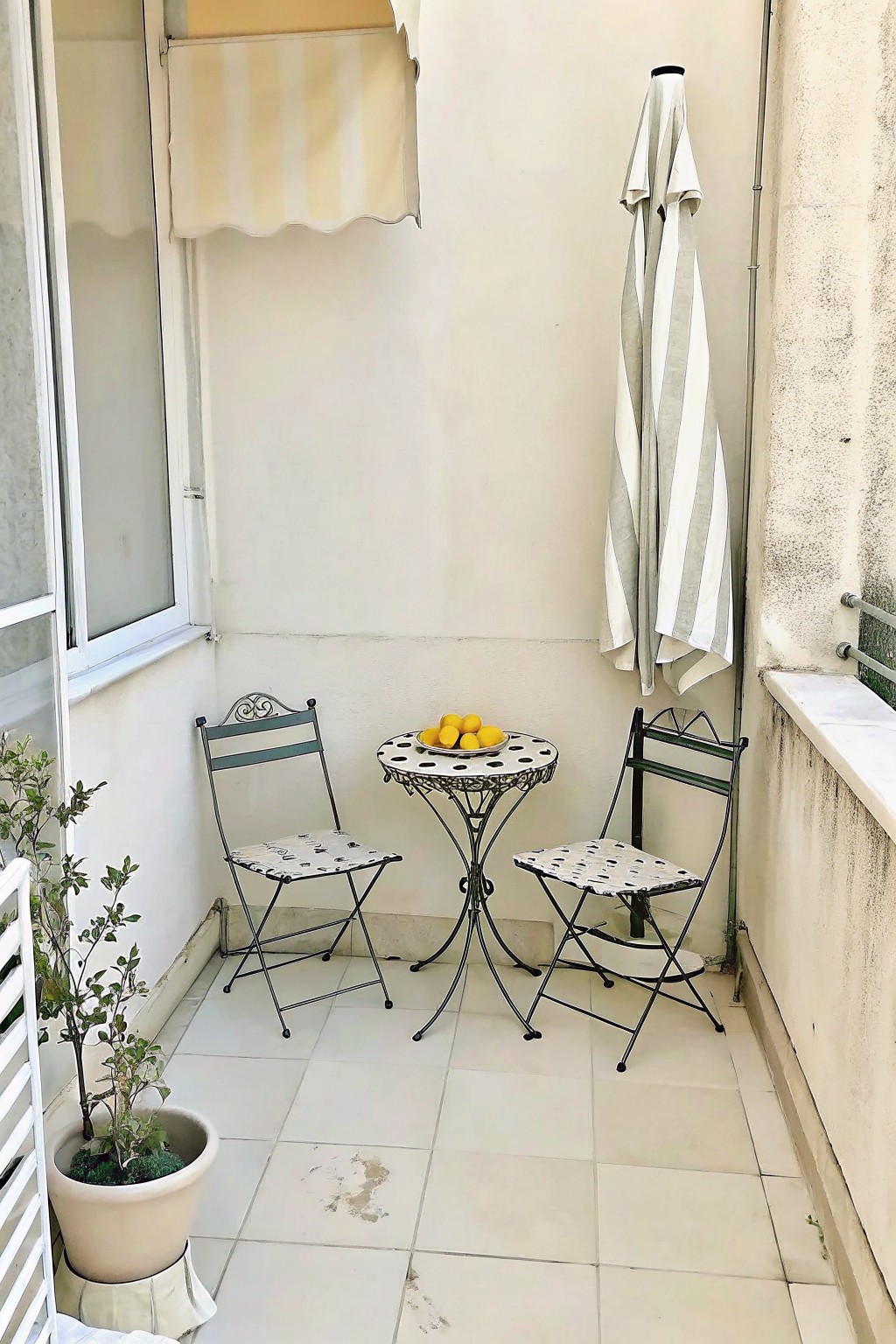 Balcony with polka dot chairs, table of lemons, striped umbrella, and potted plant.