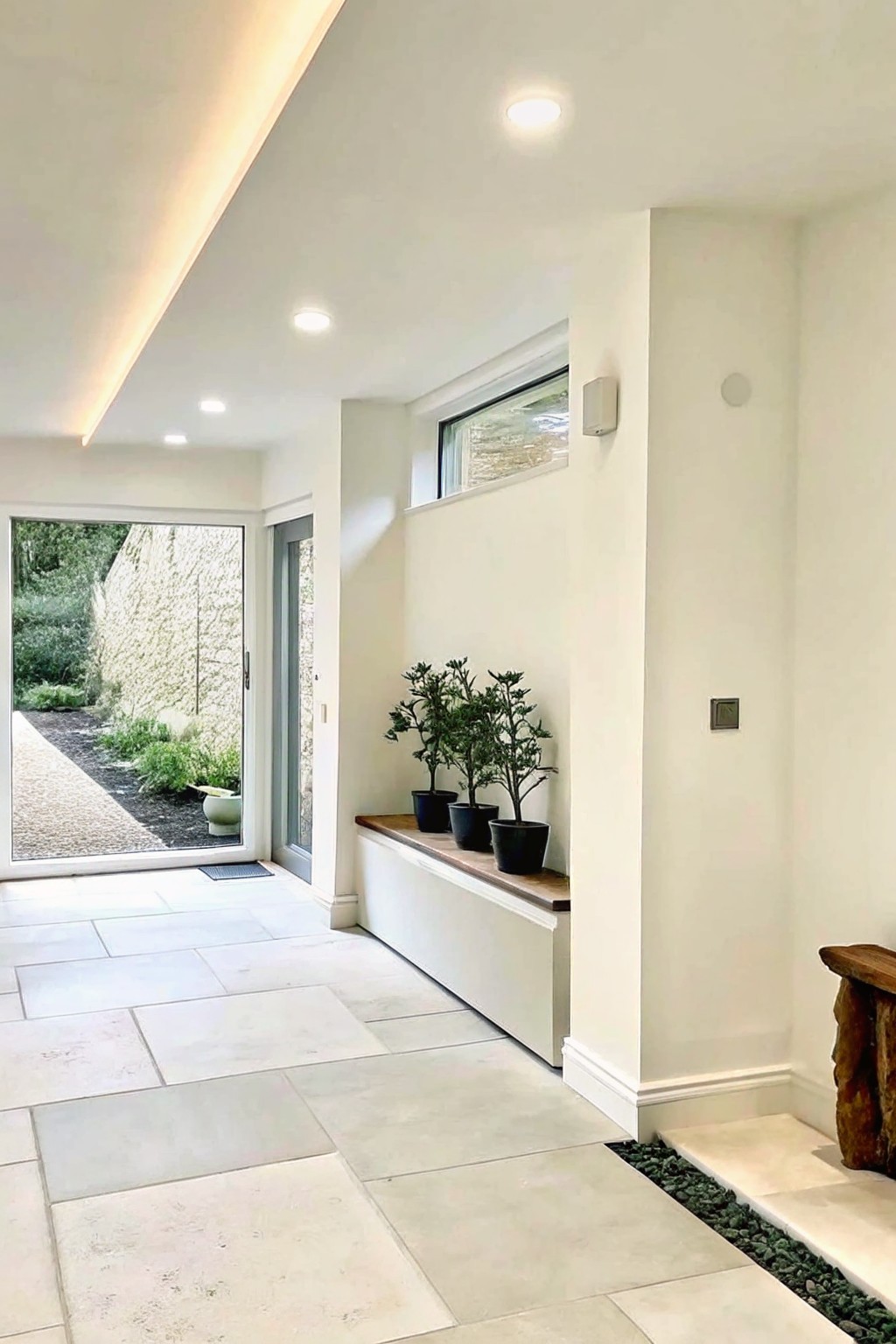 Modern white hallway with built-in bench, potted plants, and open door to garden