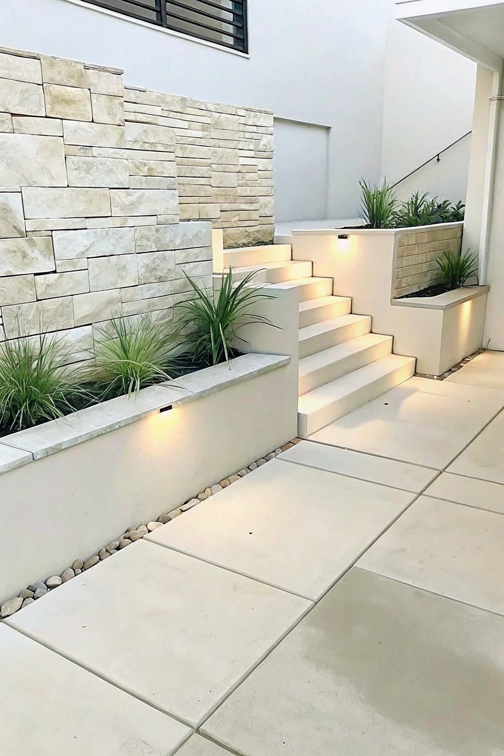 Outdoor stairs with built-in rectangular stone planters containing grasses, set against a stacked stone wall with pebble edging along the base.