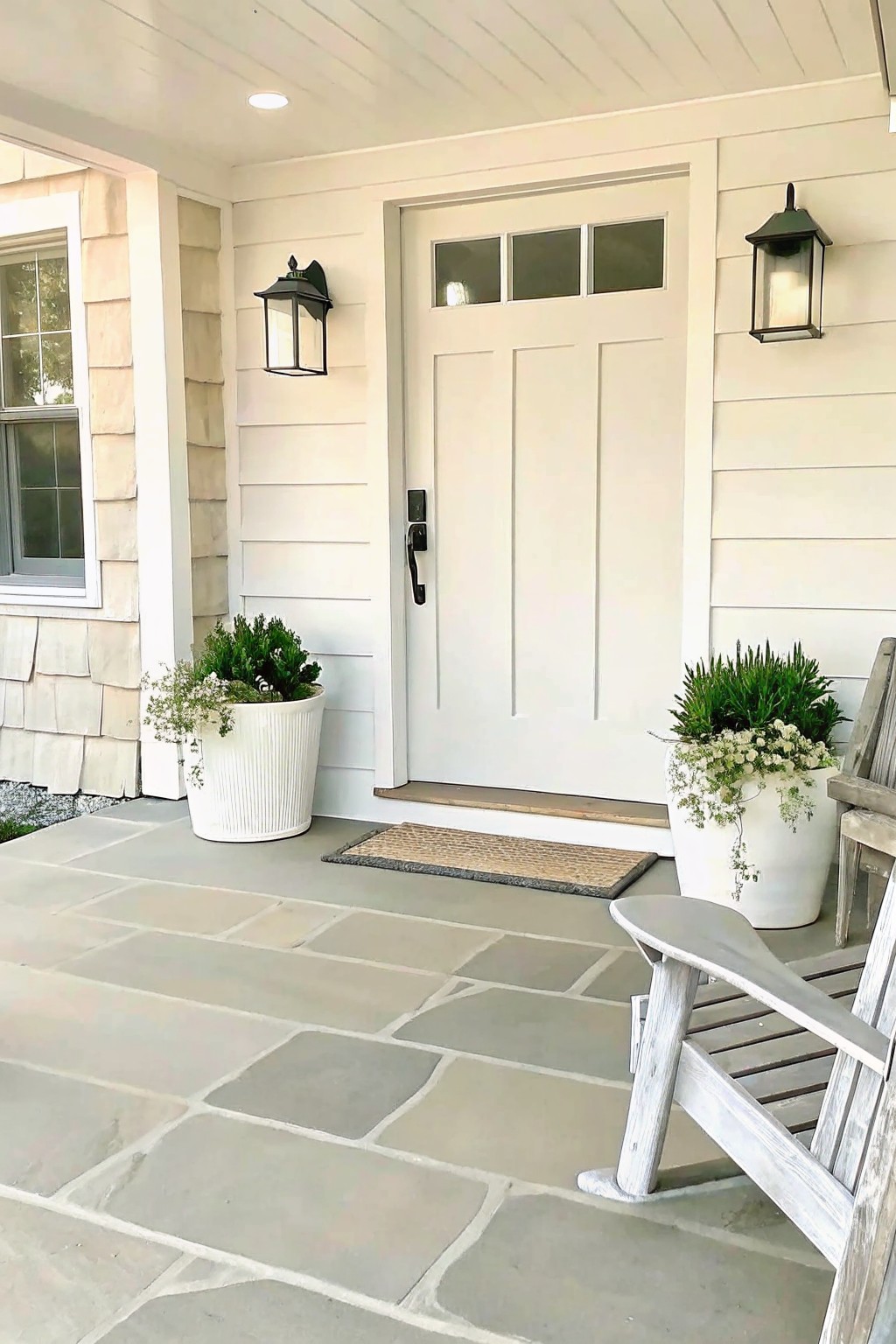 White door on stone porch with potted plants, lanterns, and wooden chair