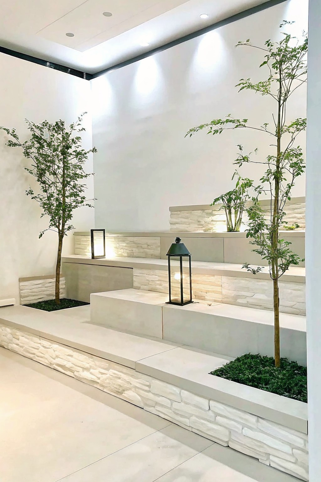 White tiered platforms with stone bases, planted trees, and a black lantern.