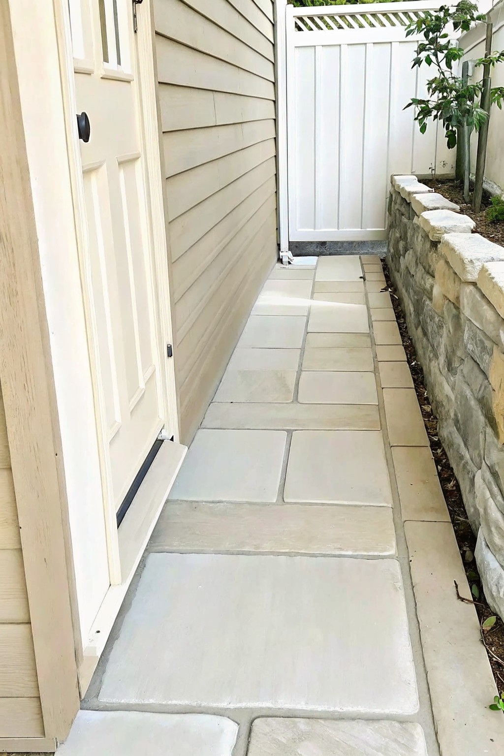 Narrow stone path beside beige house door and stone wall to white gate