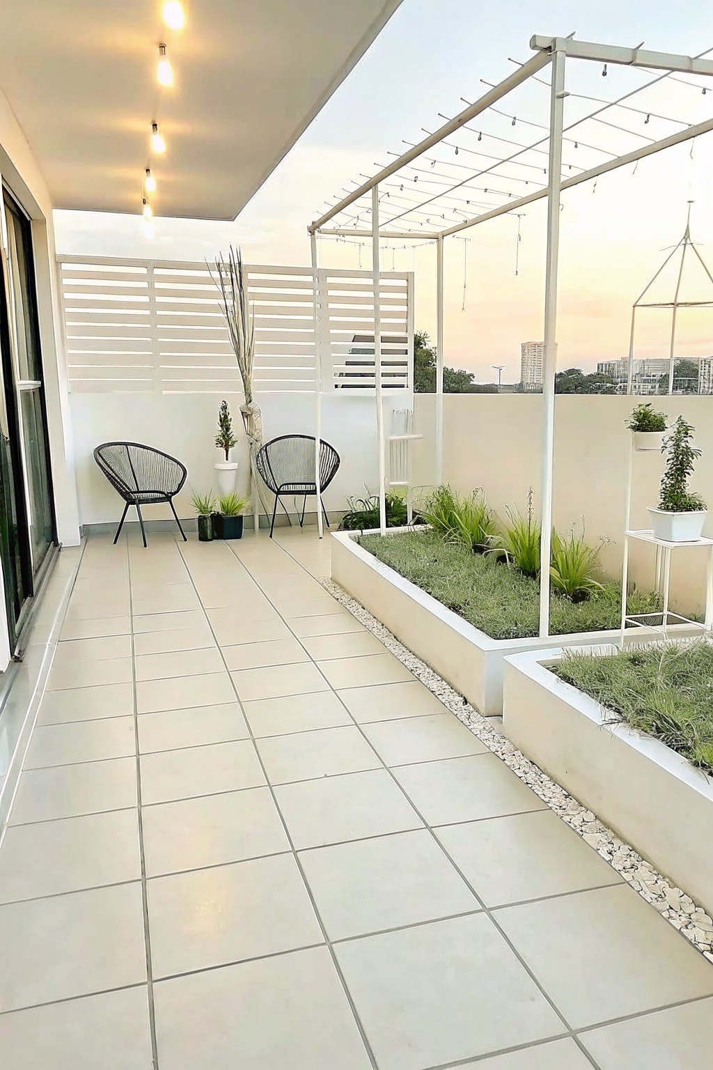 A tiled rooftop terrace with two white raised garden beds containing plants, a gravel border, black wire chairs, and a white pergola overhead.