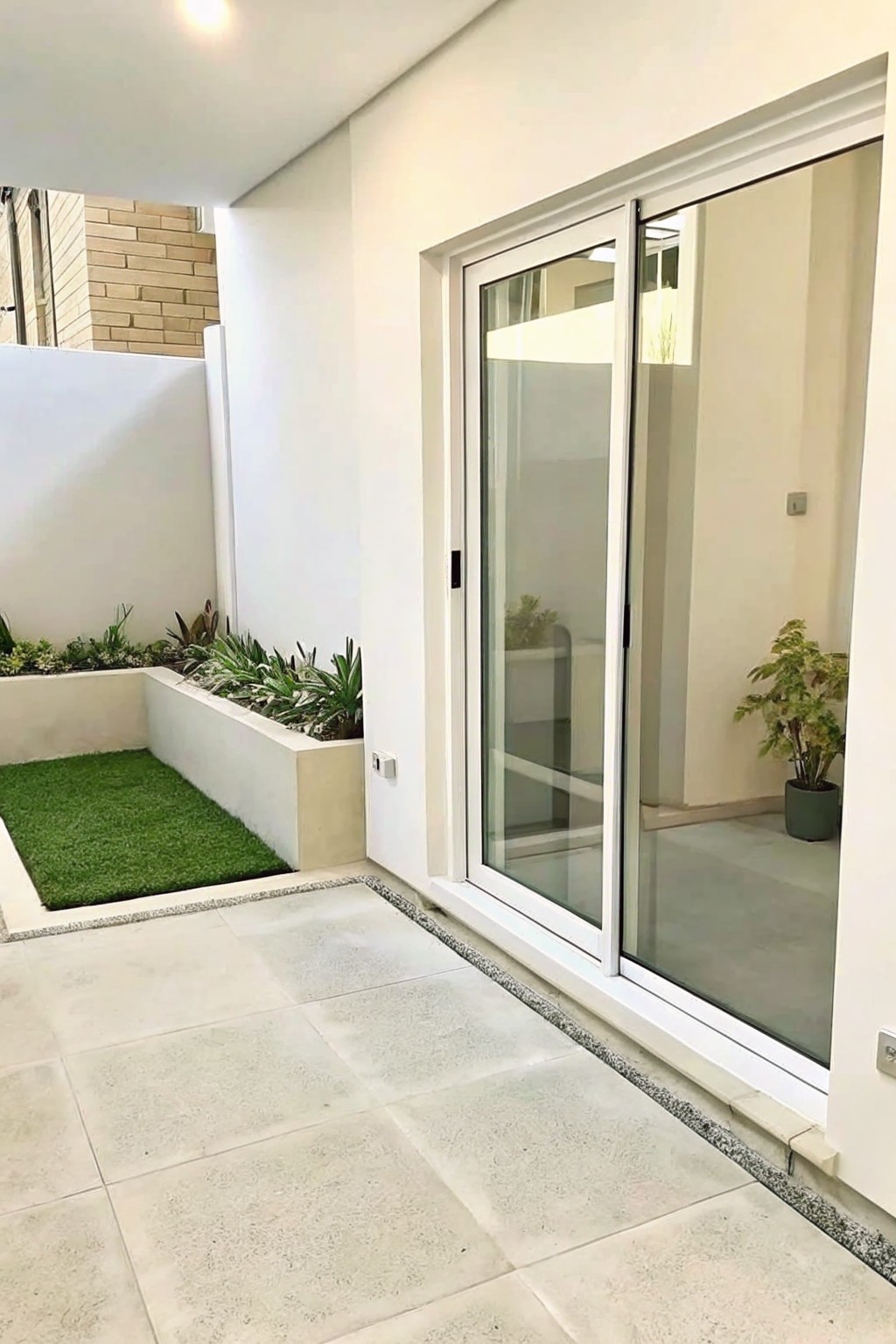Modern patio with white sliding doors, tiled floor, and raised plant bed