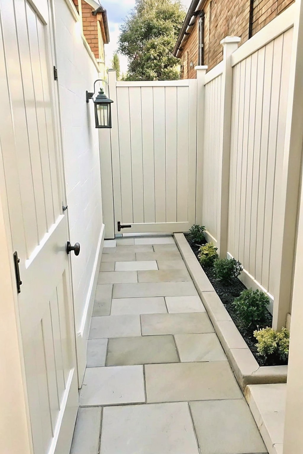 A narrow stone path between white fences with a low border and small plants along one side.