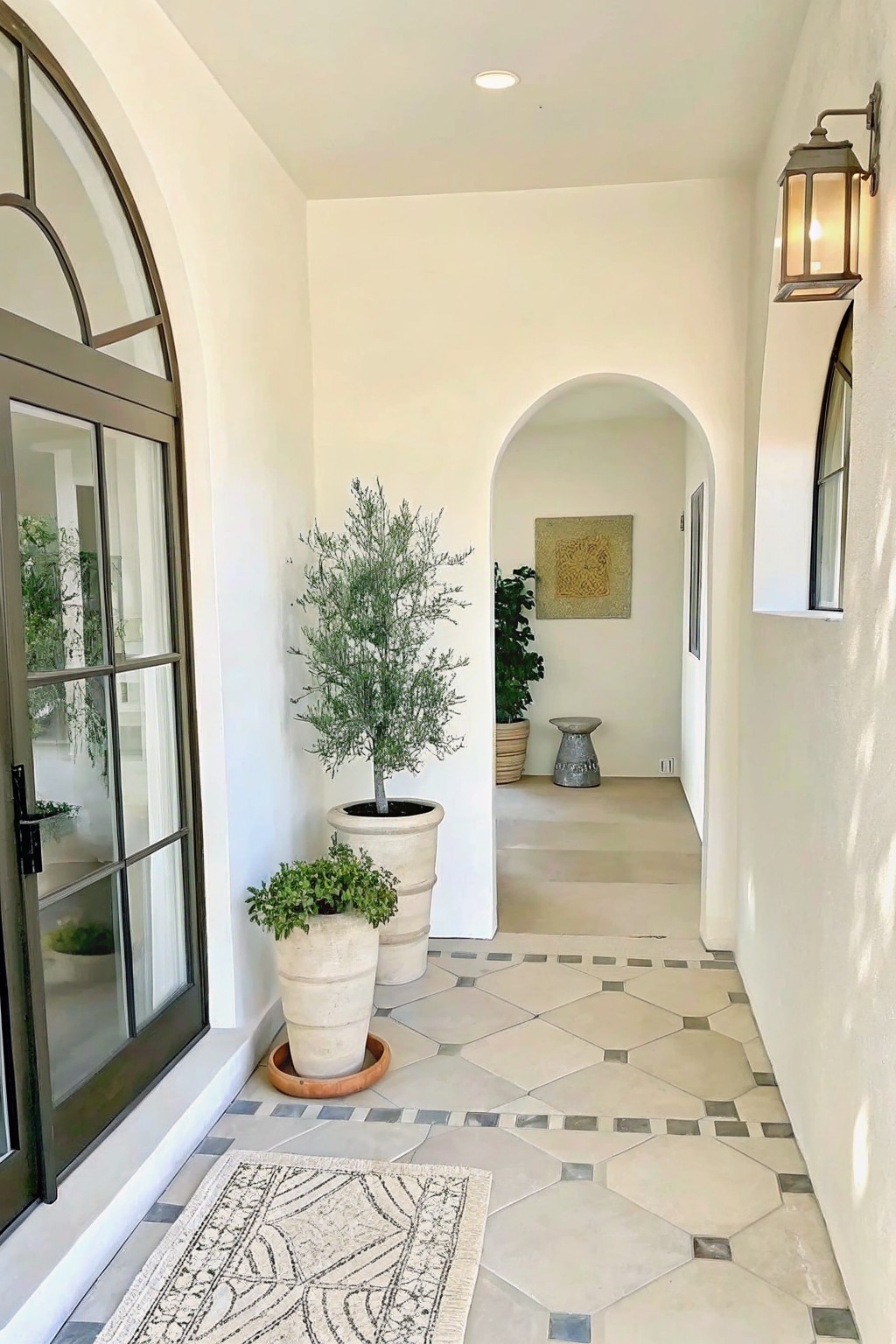 White arched hallway with potted plants, geometric tile floor, and lit lantern.