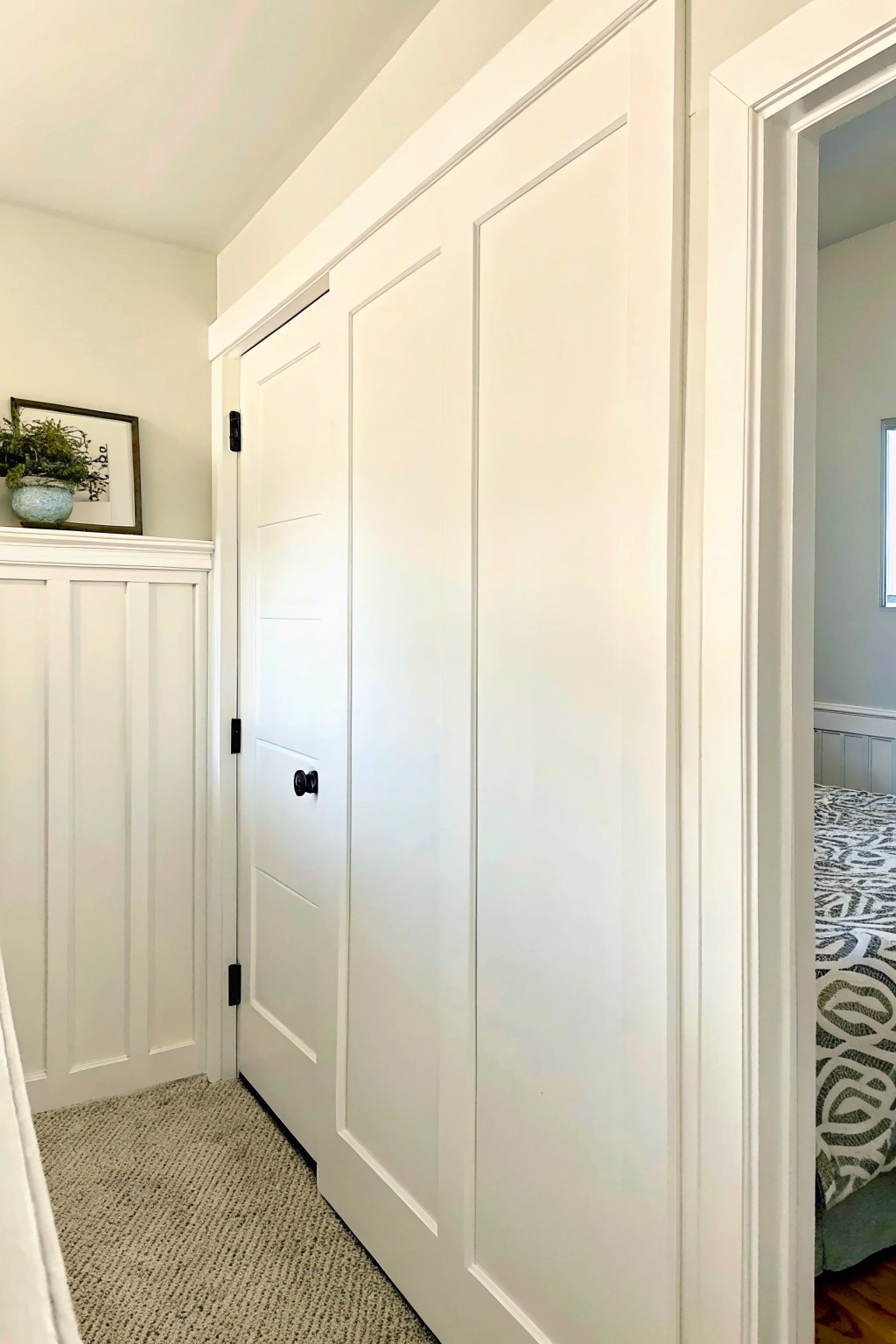 White paneled doors in hallway beside open bedroom doorway with carpeted floor